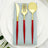 Gold cutlery set with red handles on a blue napkin atop a white plate.