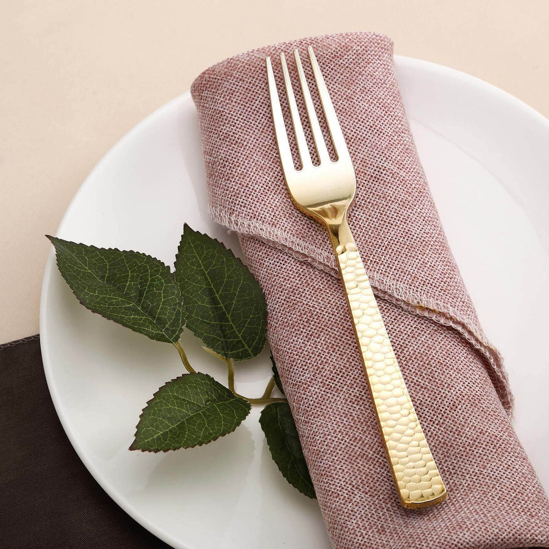 Gold fork on a pink napkin with a plate and green leaves.