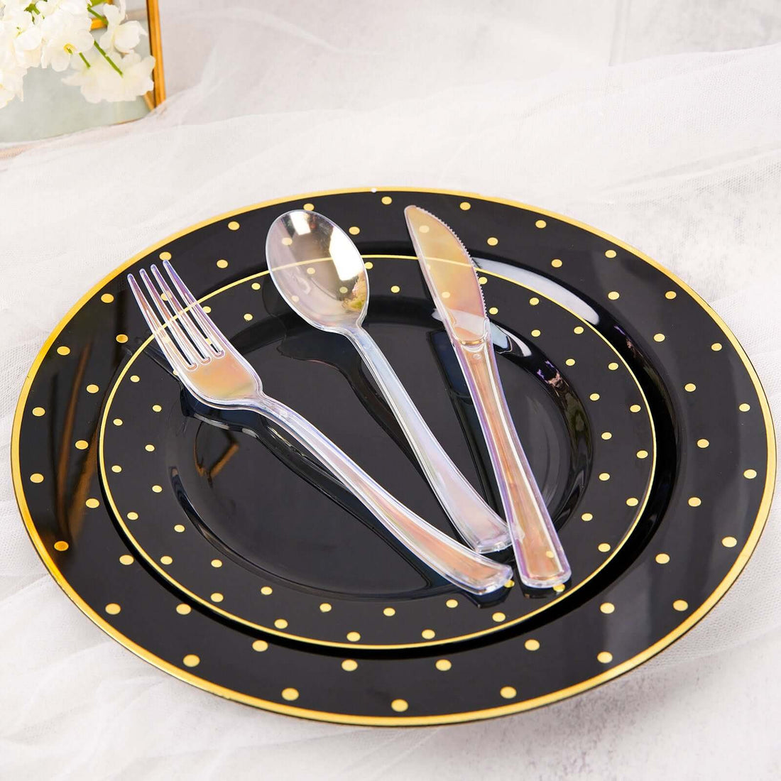 Black dinnerware set with gold polka dots, featuring plates, fork, knife, and spoon.