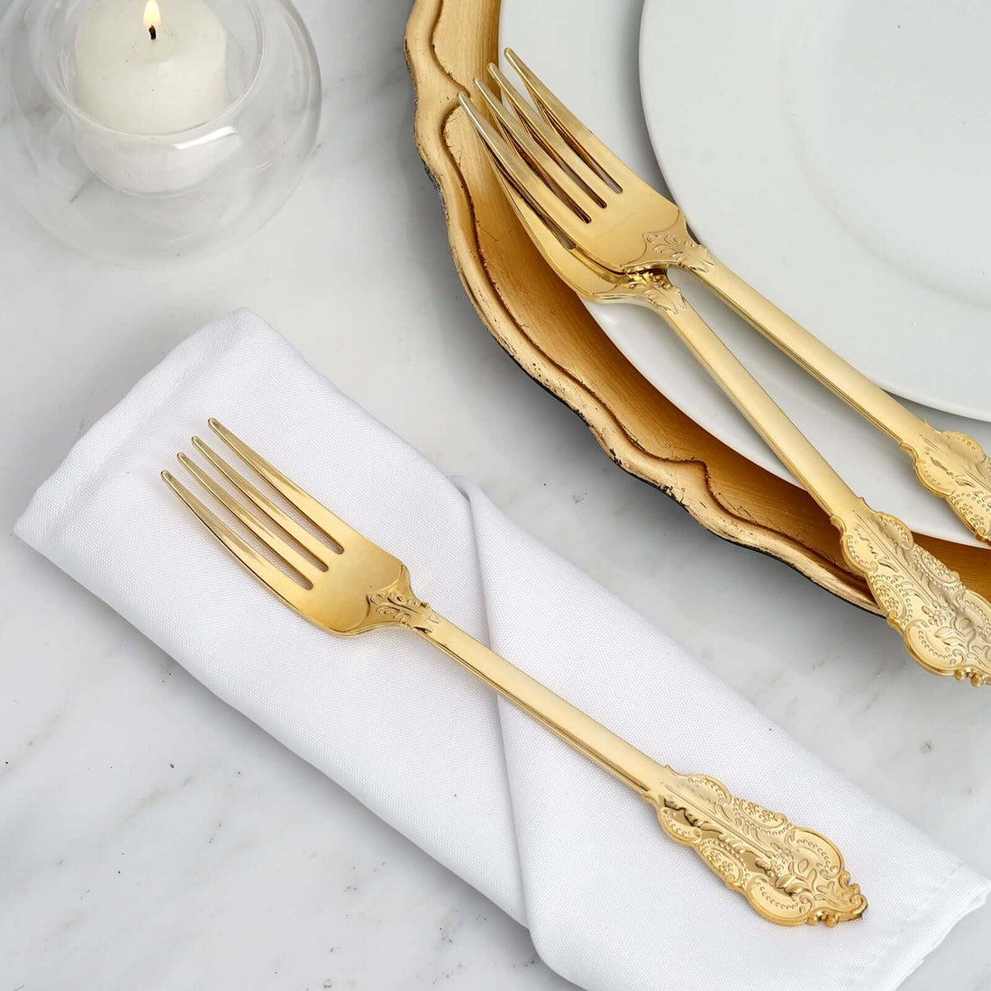 Elegant gold forks on a white napkin and gold-rimmed plate.