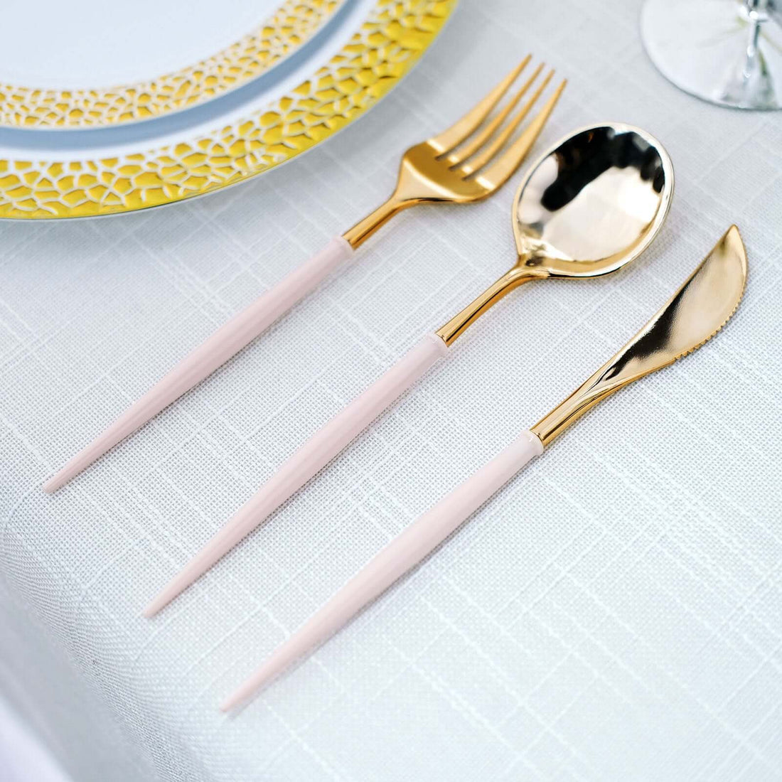 Elegant gold and pink cutlery set on a textured tablecloth.