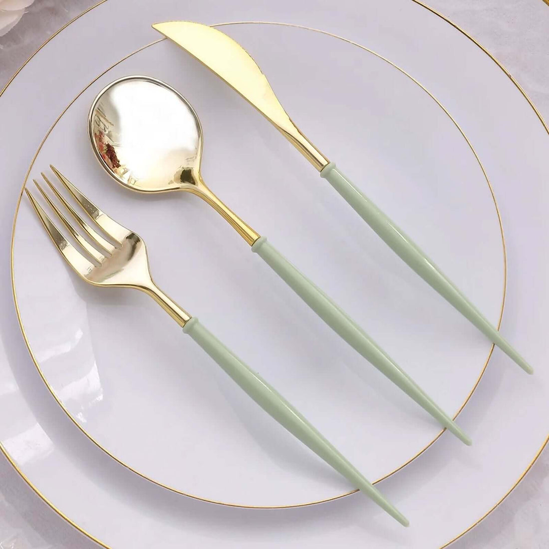 Gold and green utensils set on a white plate with golden rim.