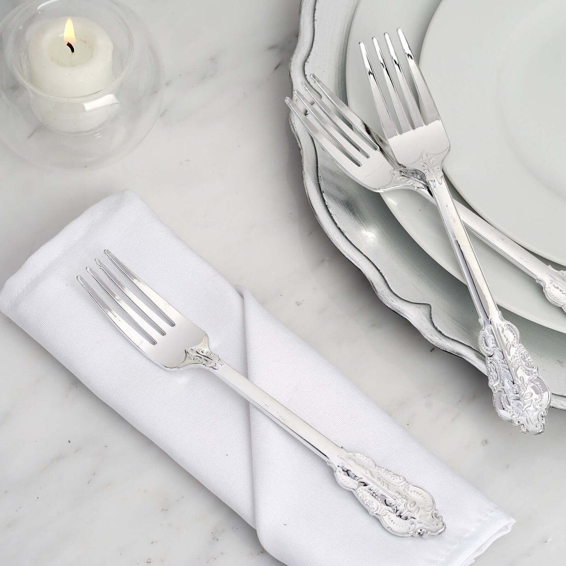Set of elegant silver forks on a white napkin with plates in the background.