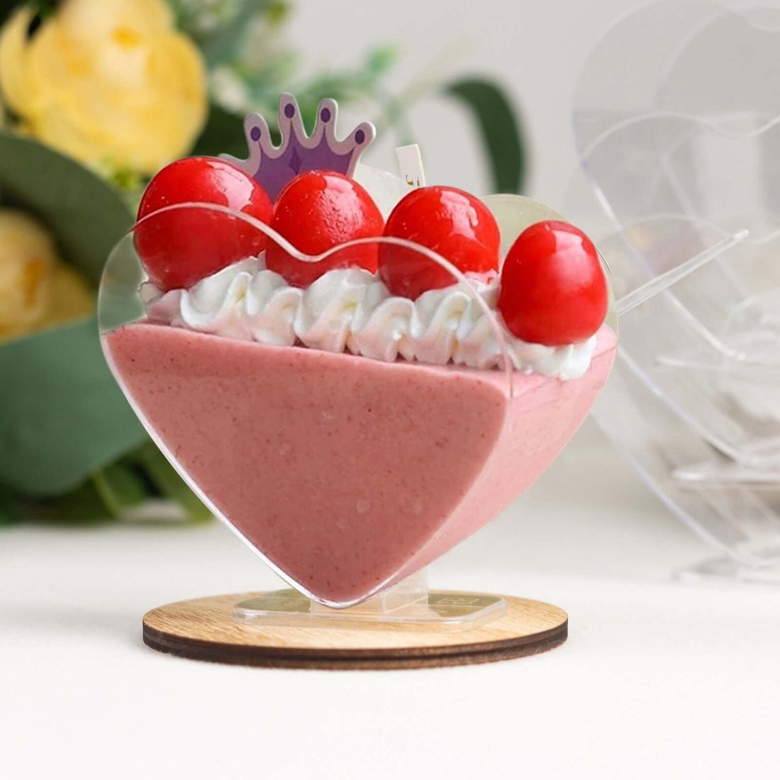 Heart-shaped dessert with whipped cream and cherries on a wooden base.