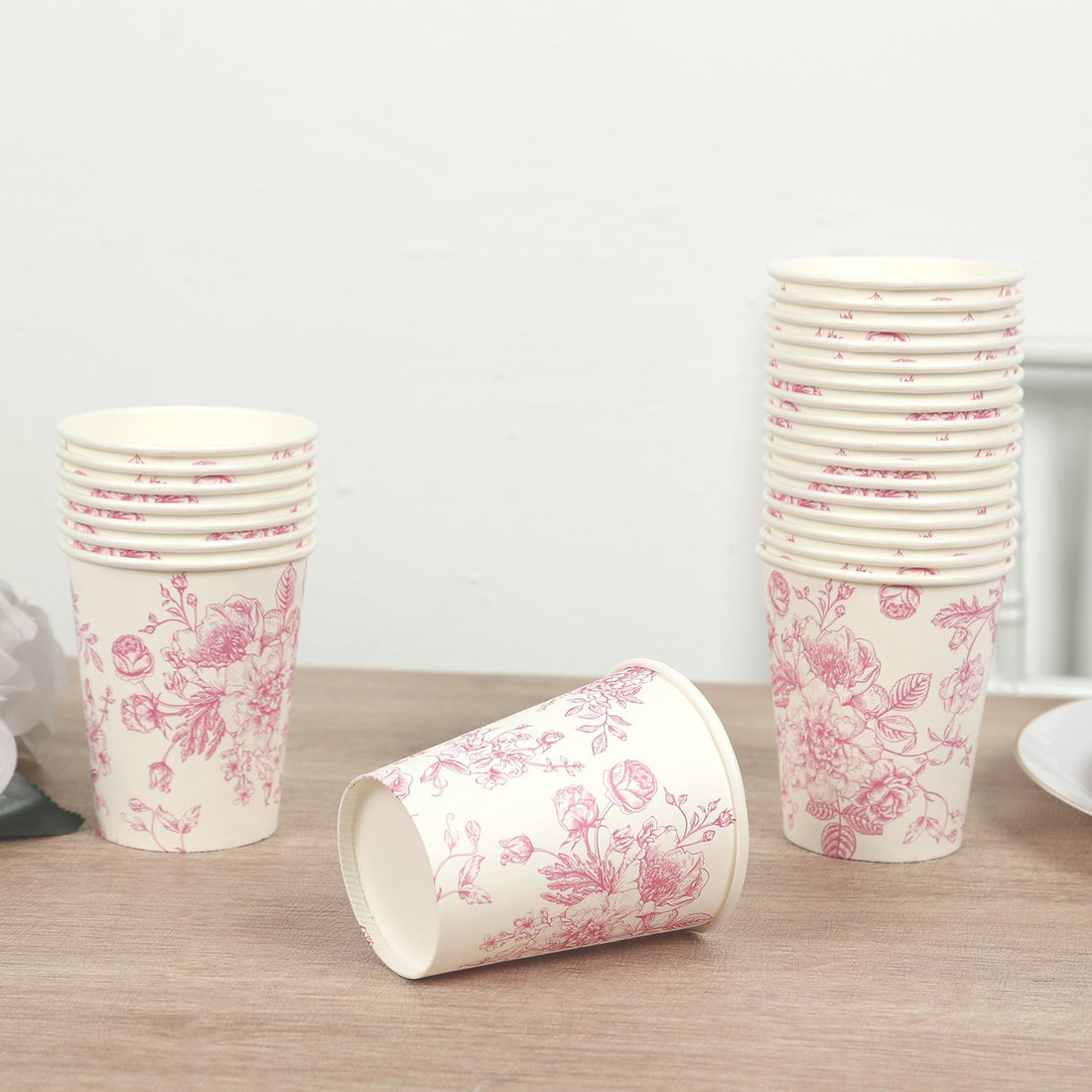 Floral paper cups stacked on a wooden table with one cup tipped over.