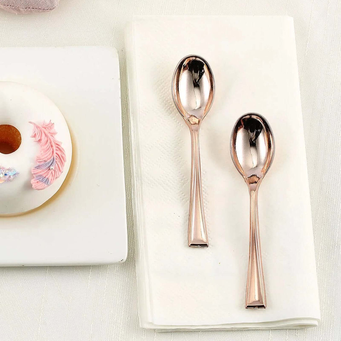 Rose gold dessert spoons on a napkin beside a donut