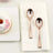 Rose gold dessert spoons on a napkin beside a donut