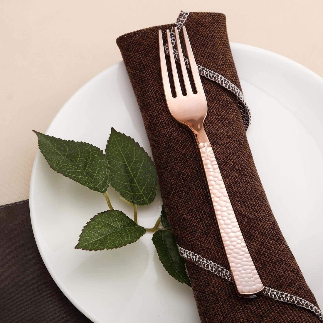 Rose gold fork on a napkin with leaves on a white plate.