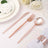 Rose gold cutlery set including knife, fork, and spoon on a table setting.
