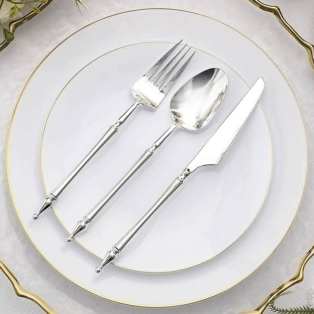 Silver cutlery set on a white plate with elegant gold rim.