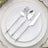 Silver cutlery set on a white plate with elegant gold rim.