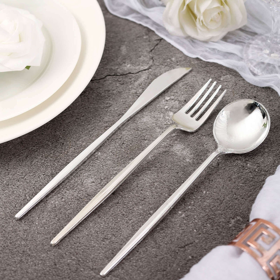 Elegant silver cutlery set including knife, fork, and spoon on a textured surface.