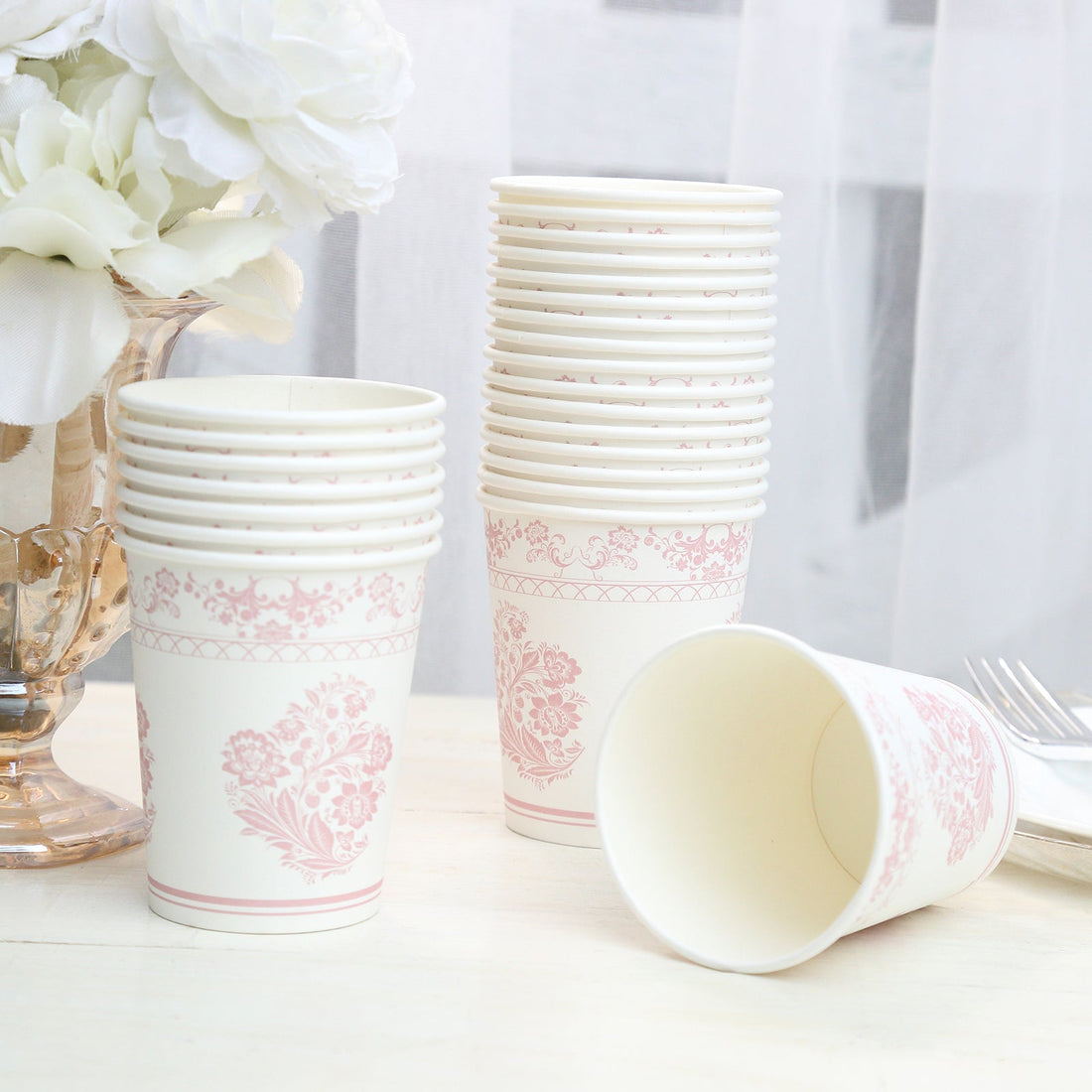 Pink floral paper cups stacked next to a vase with flowers.