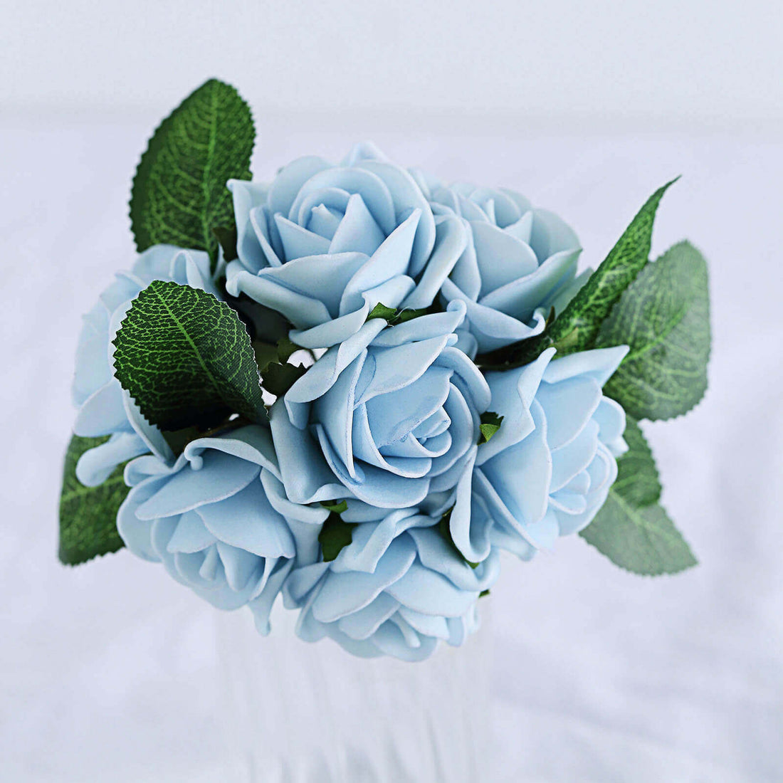 Blue rose bouquet with green leaves in a glass vase.