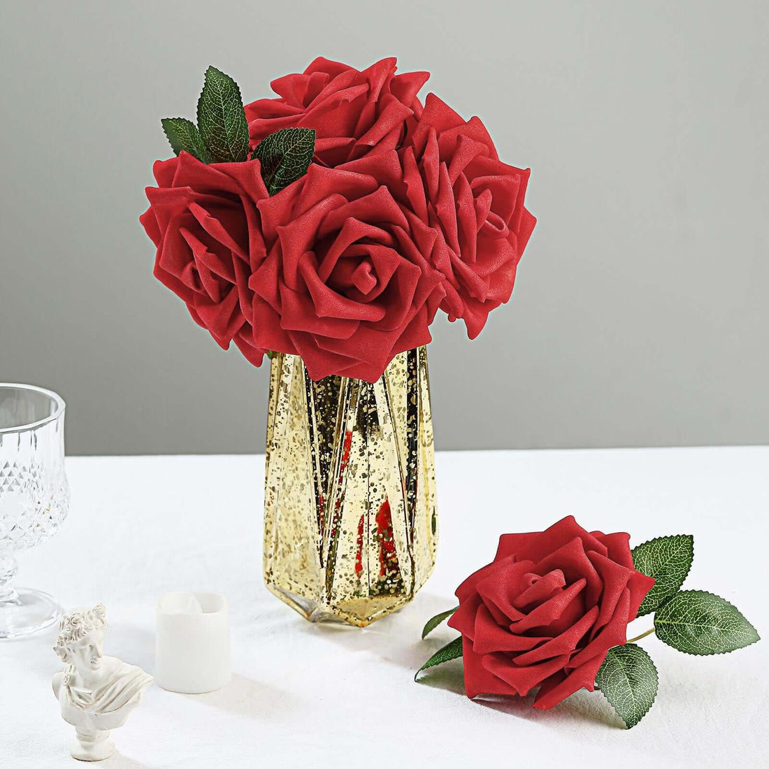 Red roses in a gold vase with a single rose beside it.