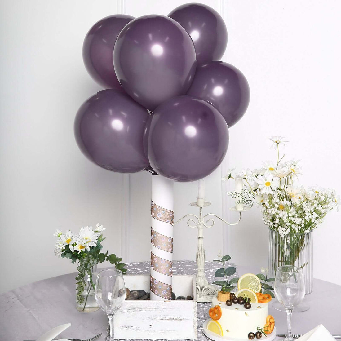 Purple balloon centerpiece with cake and flowers on a table setting.