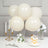 White balloons with a floral arrangement and dessert on a table setting.