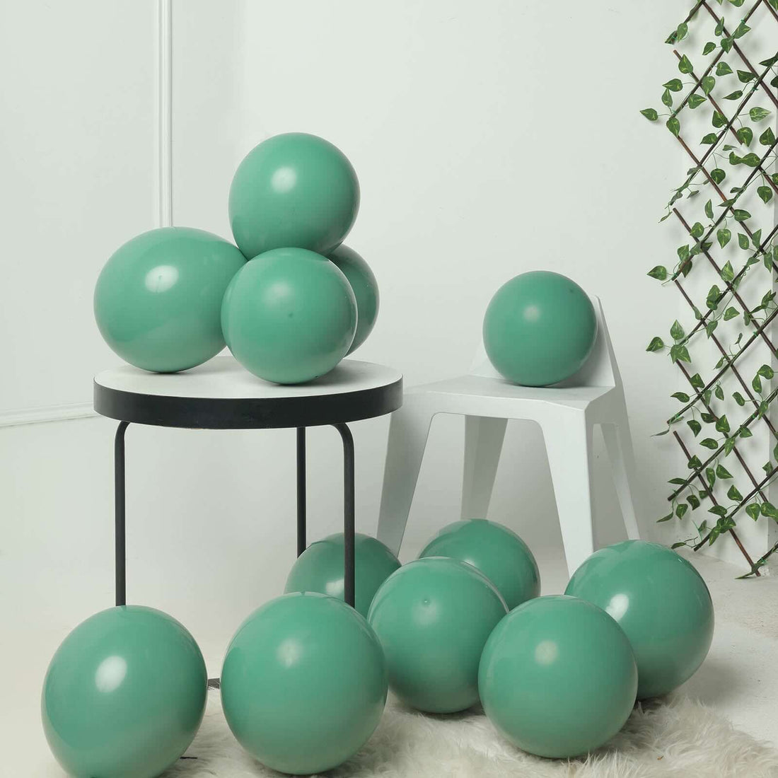 Green decorative balloons arranged around a modern chair and table in a stylish setting.