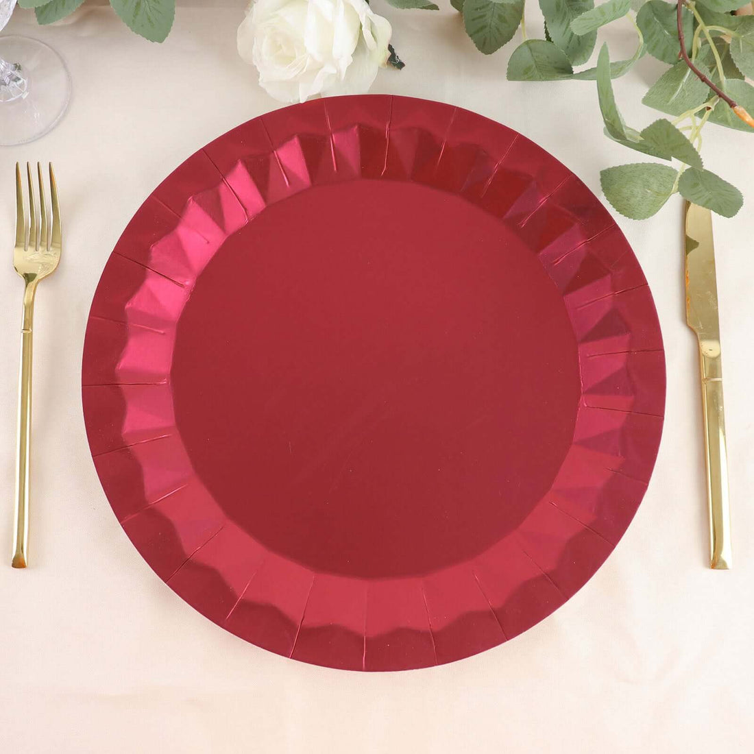 Red paper plate with scalloped edges, set on a table with gold utensils.