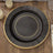 Black decorative charger plate with gold trim on a wooden table.