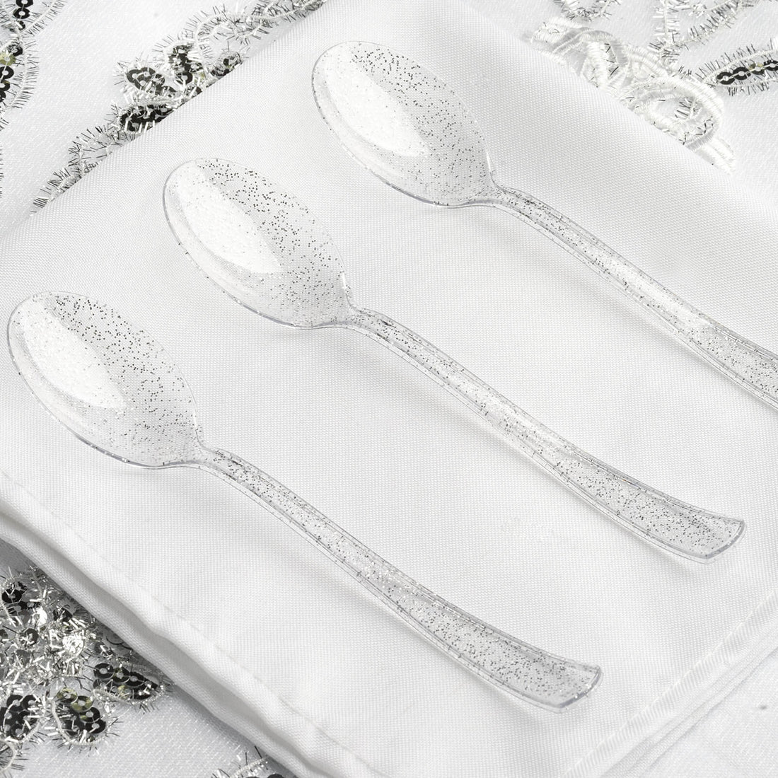 Clear plastic spoons with sparkles on a white tablecloth