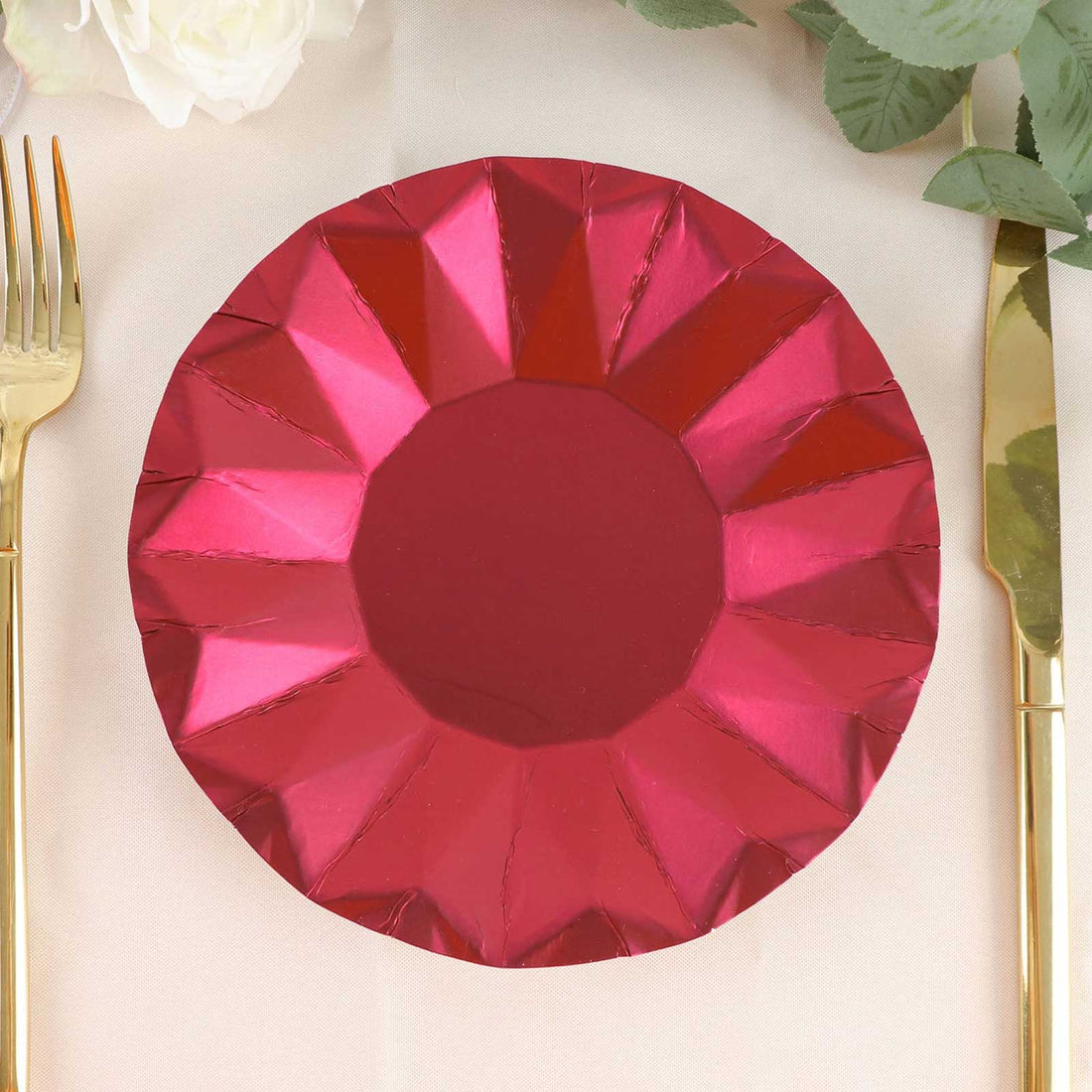 Red geometric paper plate on a table setting with gold cutlery.
