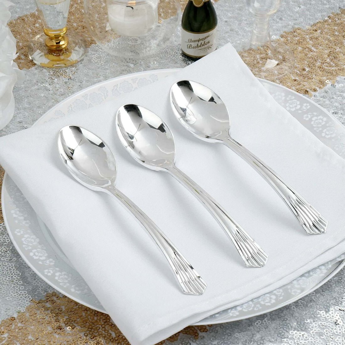 Three elegant silver spoons resting on a white napkin on a decorated table.