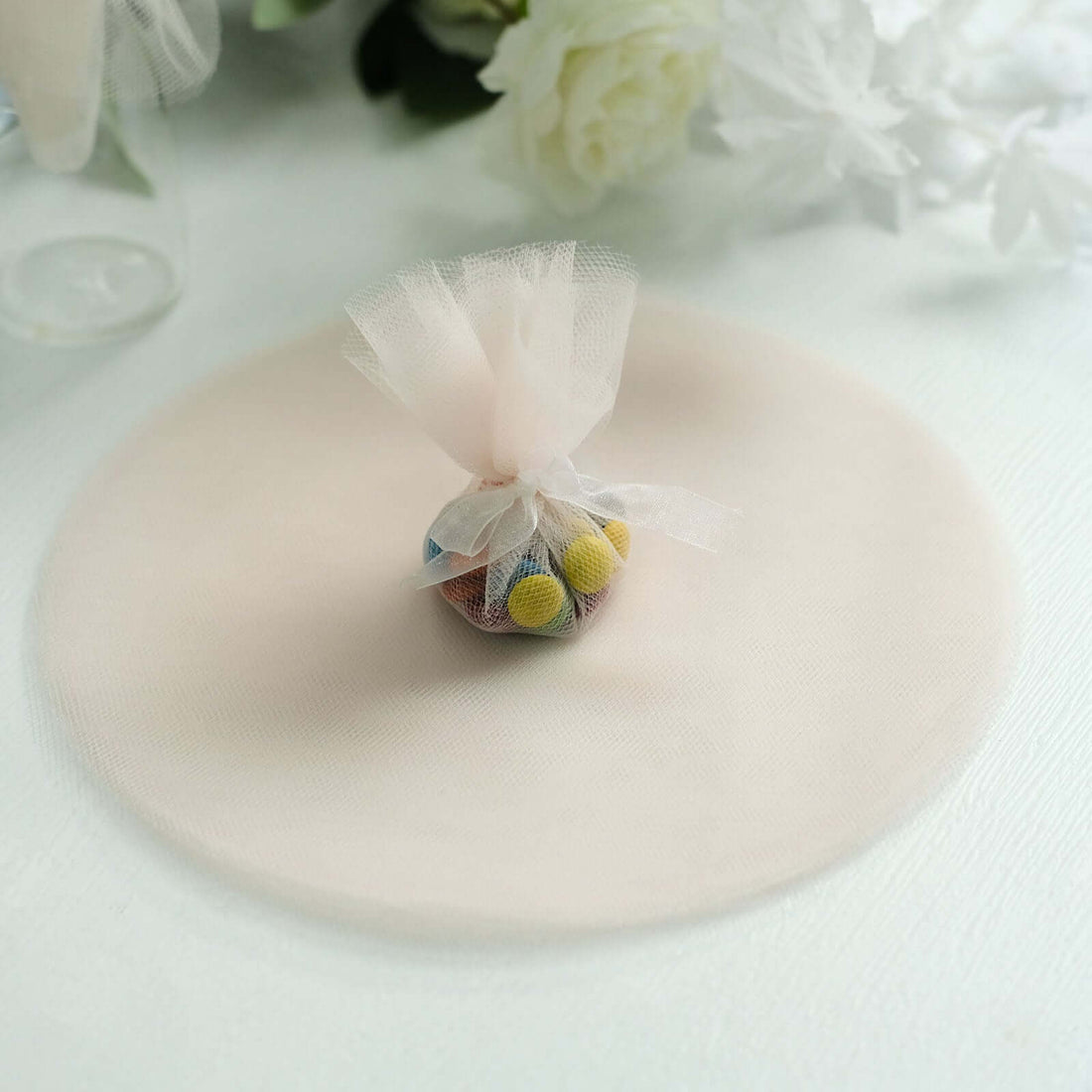 Colorful candy in a tulle bag on a soft, round fabric backdrop.
