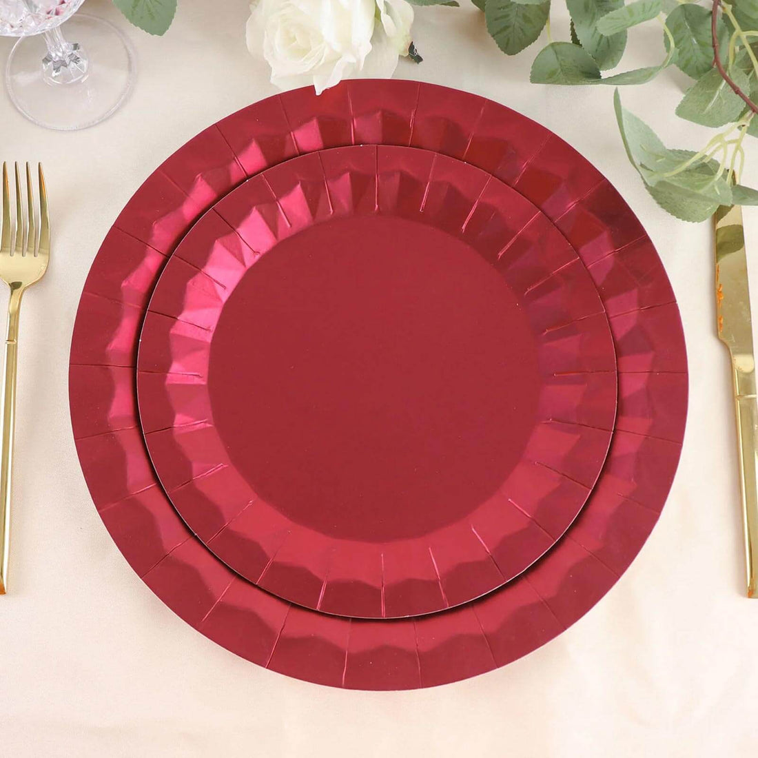 Red disposable plates stacked on a table with gold cutlery and floral decor.