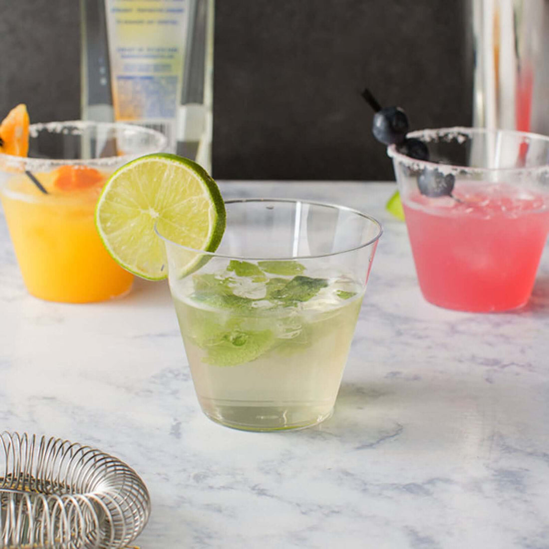Refreshing cocktails in clear glasses with fruit garnishes on a marble surface.