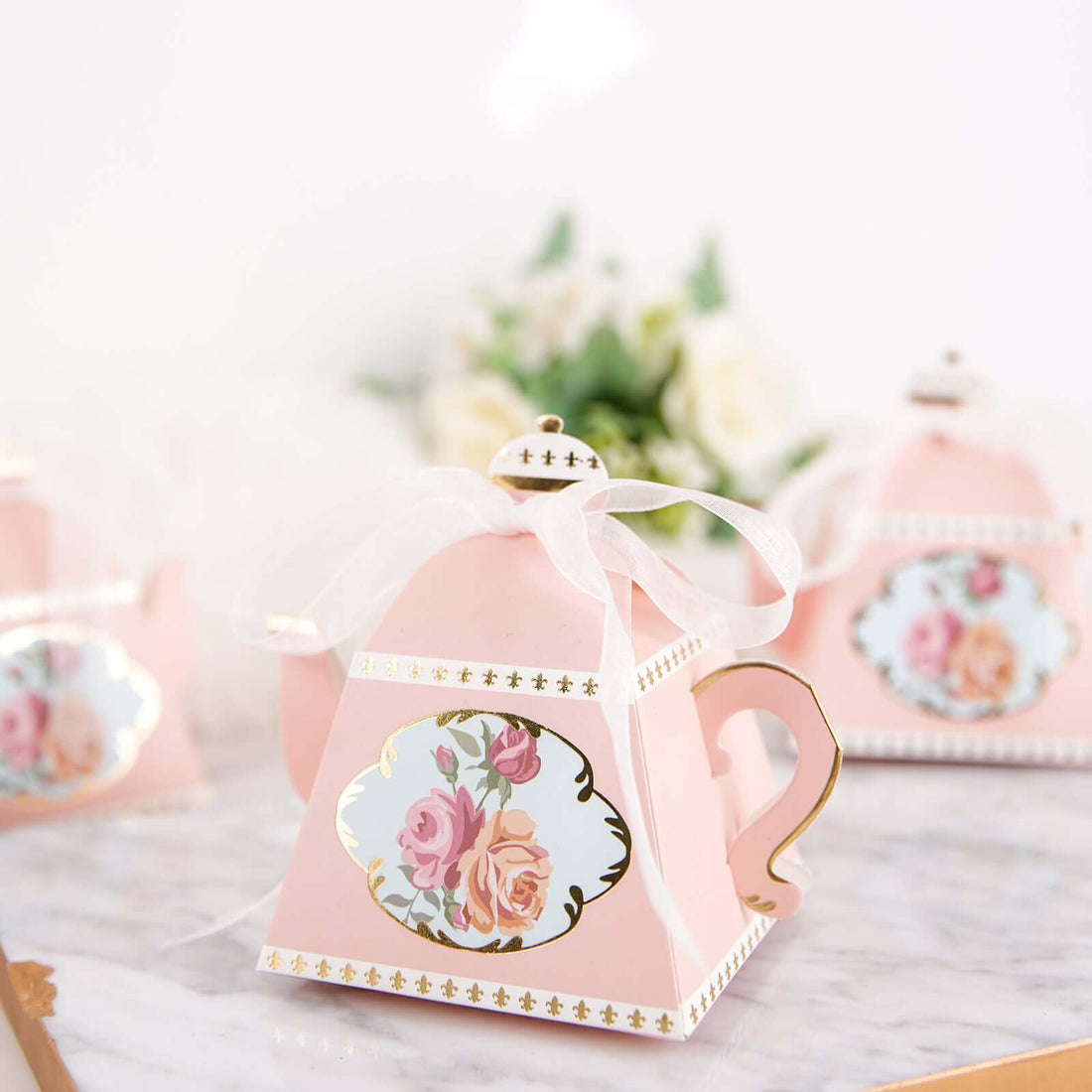 Pink floral tea party favor boxes with gold accents and ribbon.