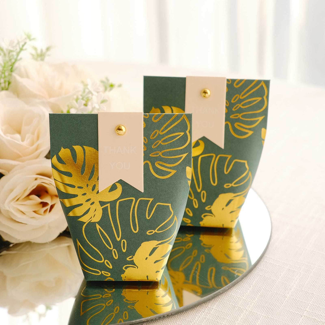 Elegant green and gold thank you favor boxes on a reflective surface.