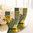 Elegant green and gold thank you favor boxes on a reflective surface.