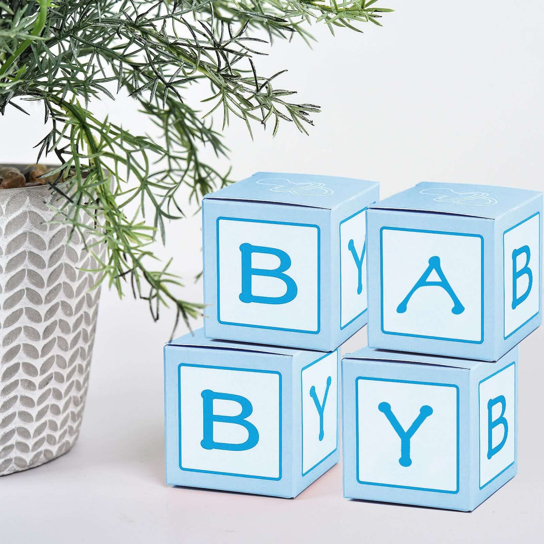 Blue baby blocks stacked next to a decorative plant.