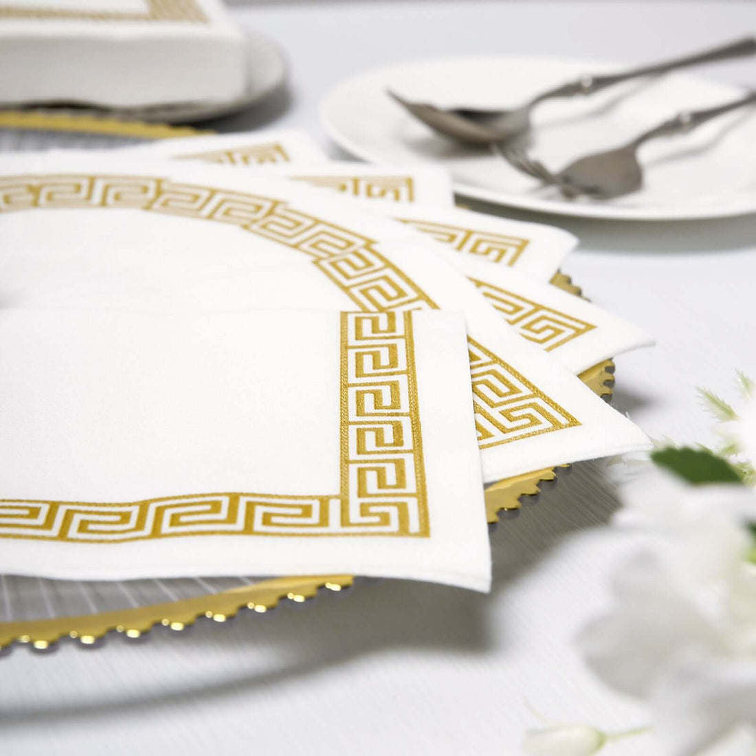 Elegant white napkins with gold Greek key design on a dining table.