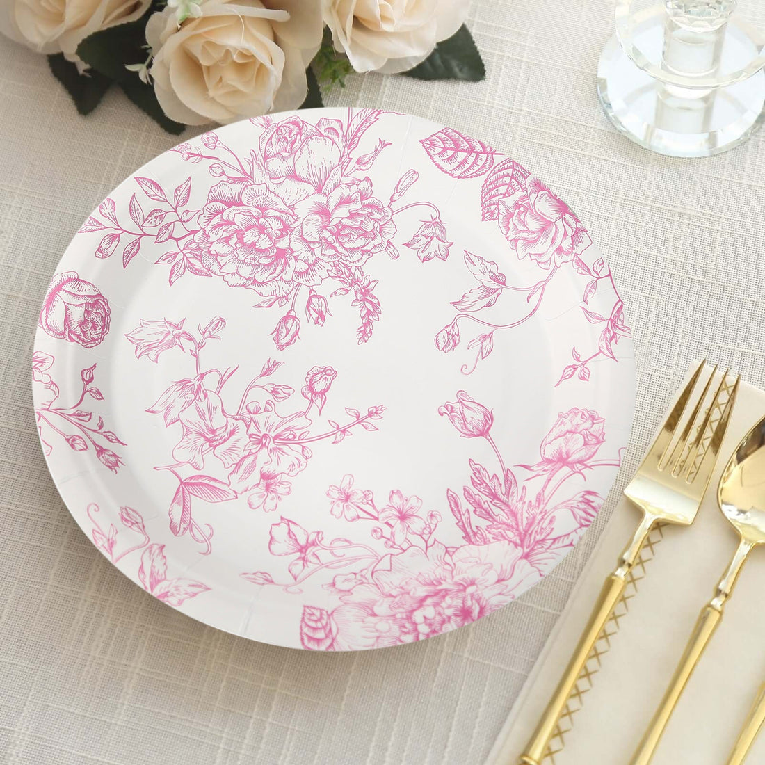 Floral patterned paper plate with gold utensils on a textured table setting.
