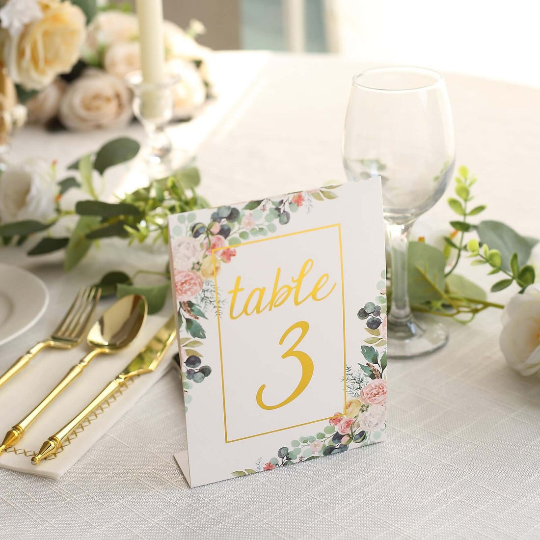 Floral table number sign with gold lettering on a dining table setting.