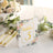 Floral table number sign with gold lettering on a dining table setting.