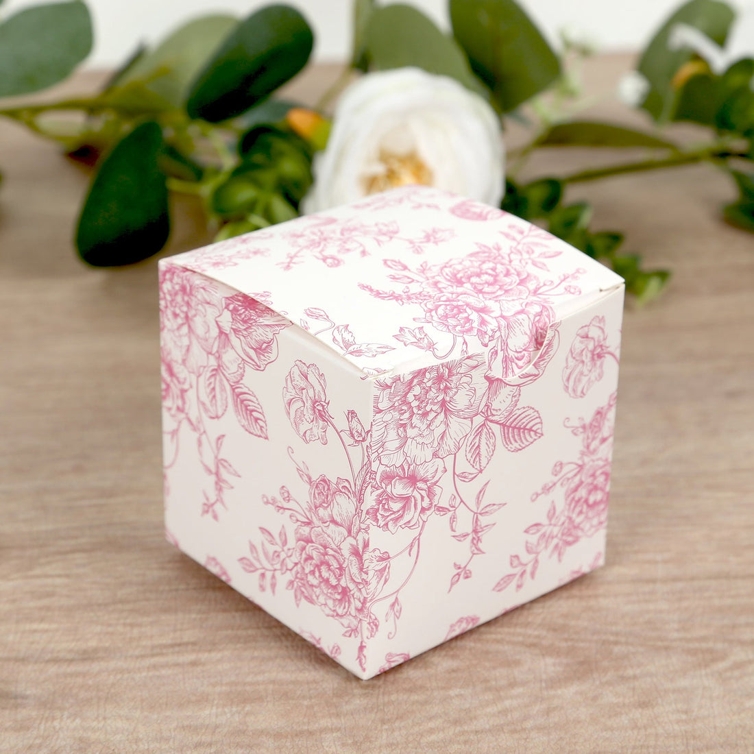 Floral-patterned gift box on a wooden surface with greenery