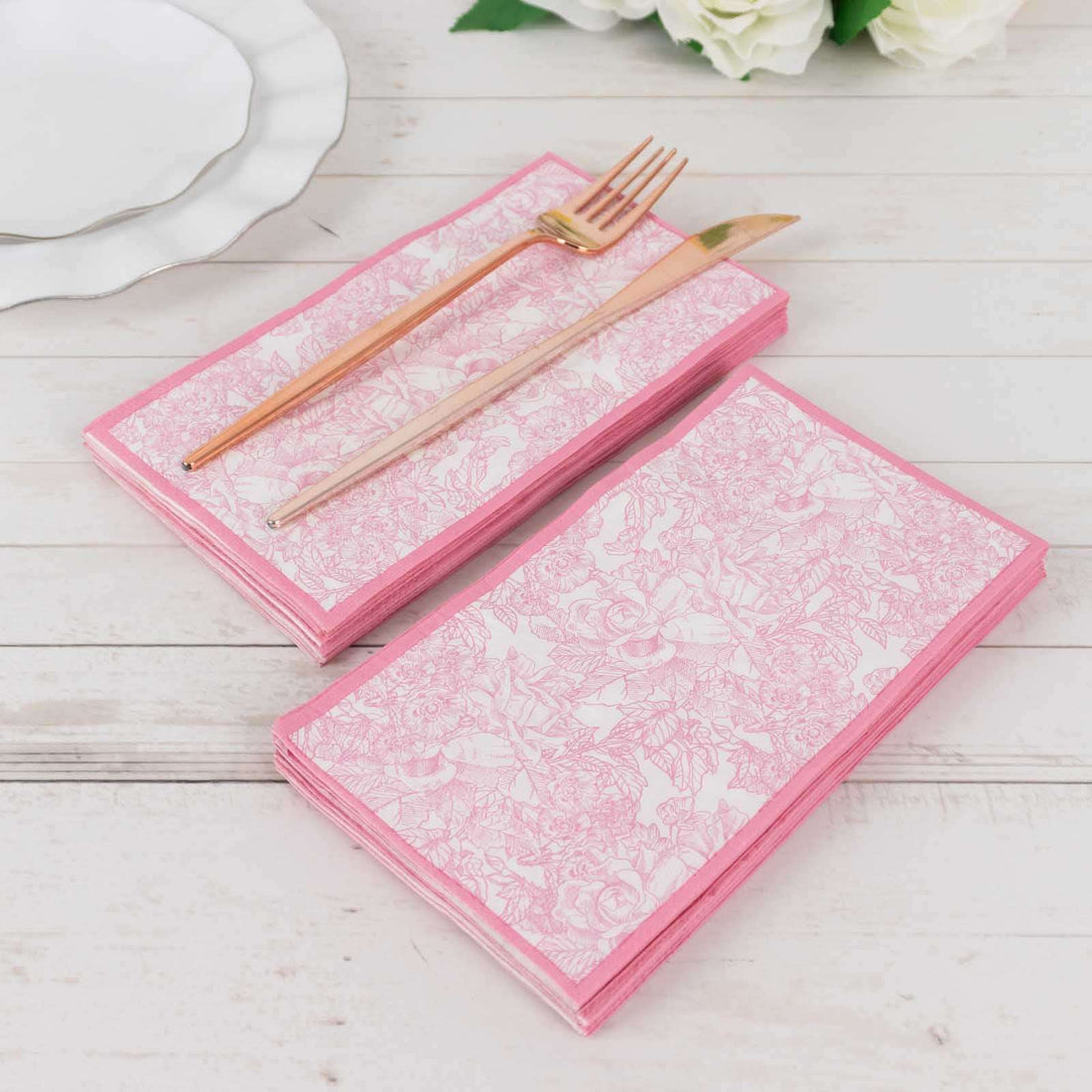 Pink floral patterned napkins with gold fork and knife on a wooden table.