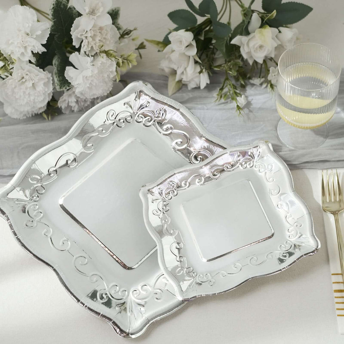 Elegant silver serving platters with intricate designs on a neutral table setting.