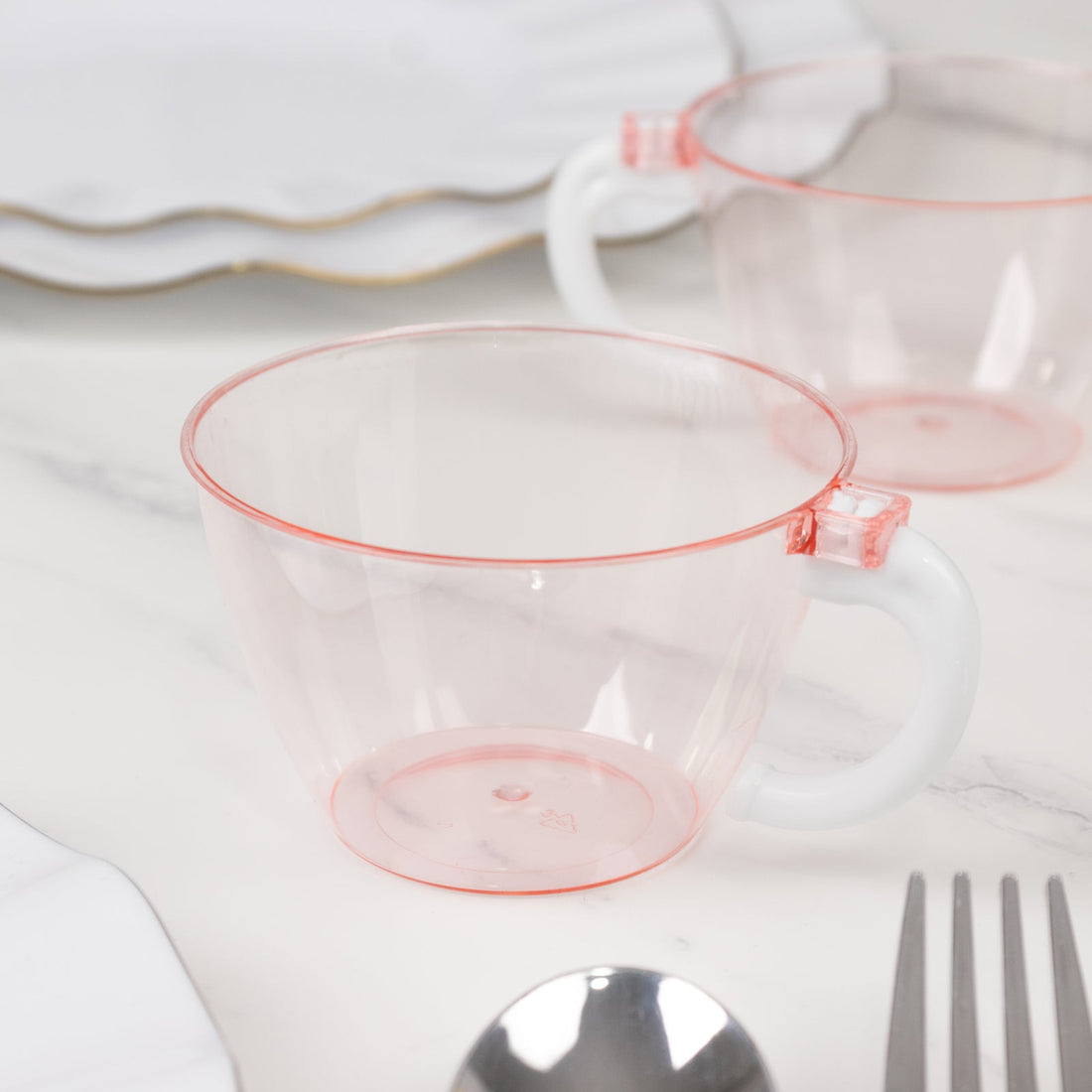Pink transparent cup with white handle on marble surface.