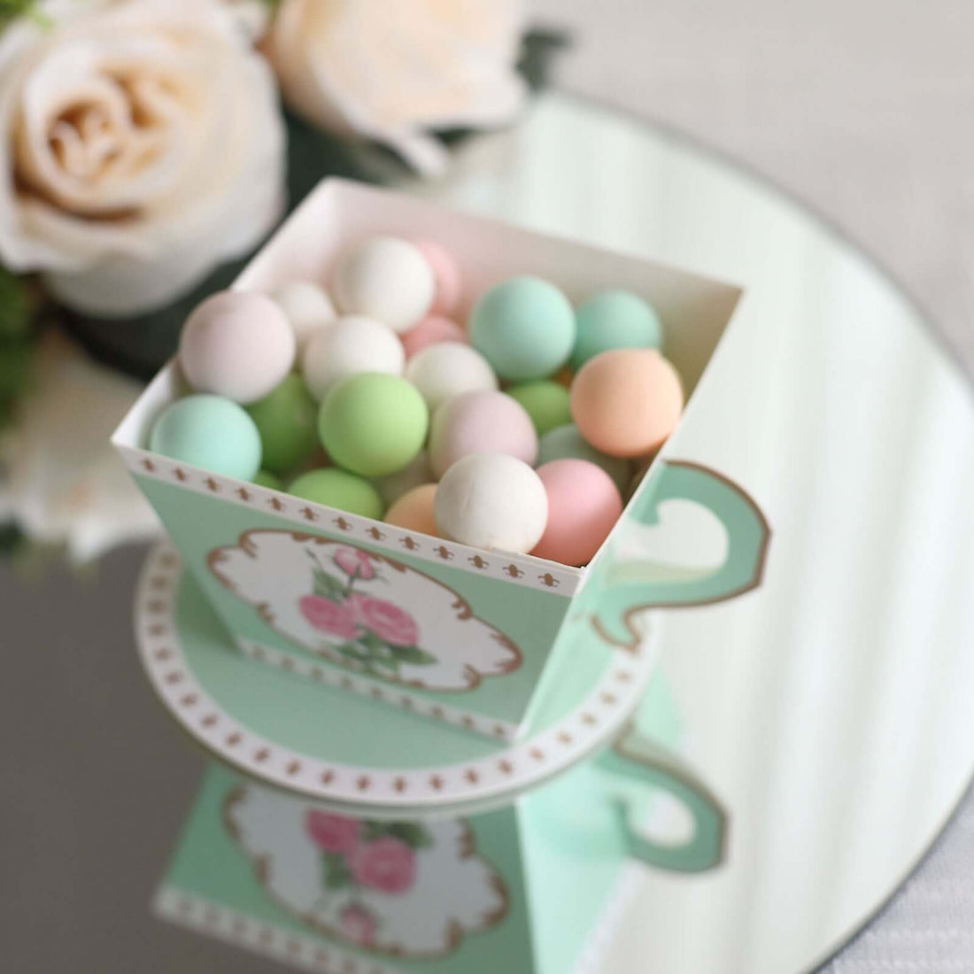 Pastel-colored candy balls in decorative cup on mirrored surface.