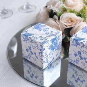Floral patterned gift boxes on a mirrored surface with roses in the background.