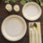 Elegant gold-accented dinnerware set with plates and cutlery on a rustic wooden table.
