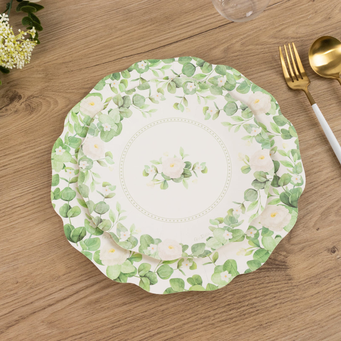 Floral decorative plate on wooden table with gold and white utensils.