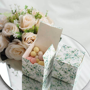 Decorative gift box with pastel candies, surrounded by flowers on a reflective surface.