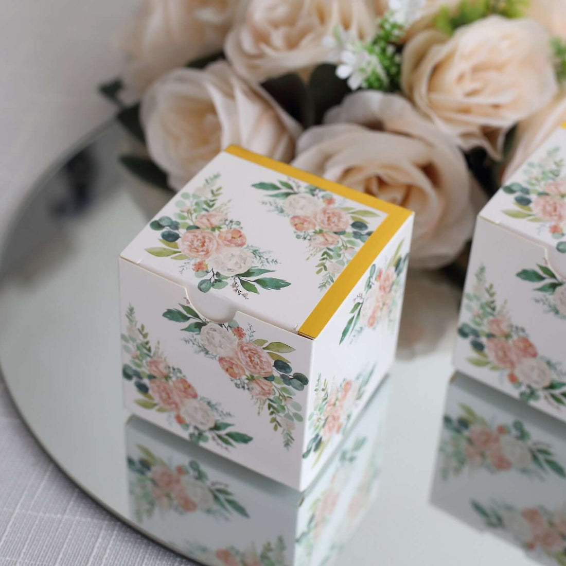 Floral gift box on a mirrored surface with roses in the background.