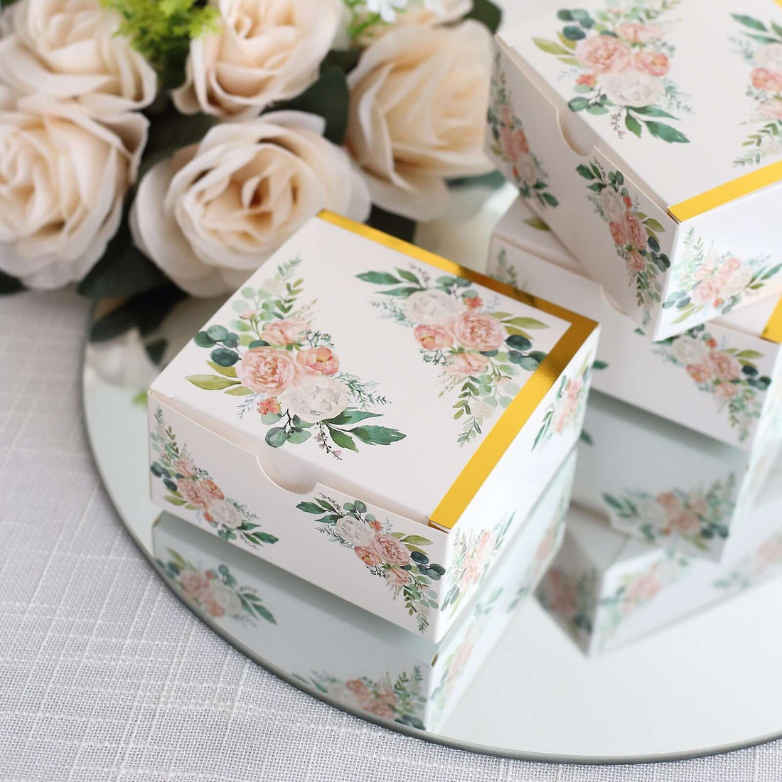 Floral gift boxes displayed on a mirrored surface with roses in the background.