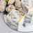 Floral gift boxes displayed on a mirrored surface with roses in the background.